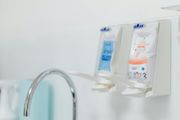 Two medical solution bags mounted on a wall near a faucet. Blue and orange labels.