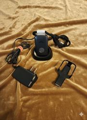 A black phone charger, a charging cradle, and a belt clip sit on a gold-colored fabric.