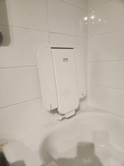 White, folding bathtub seat attached to tiled wall above a tub.