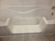 White walk-in bathtub with a step for entry, gray tile floor, water fixture on the right.