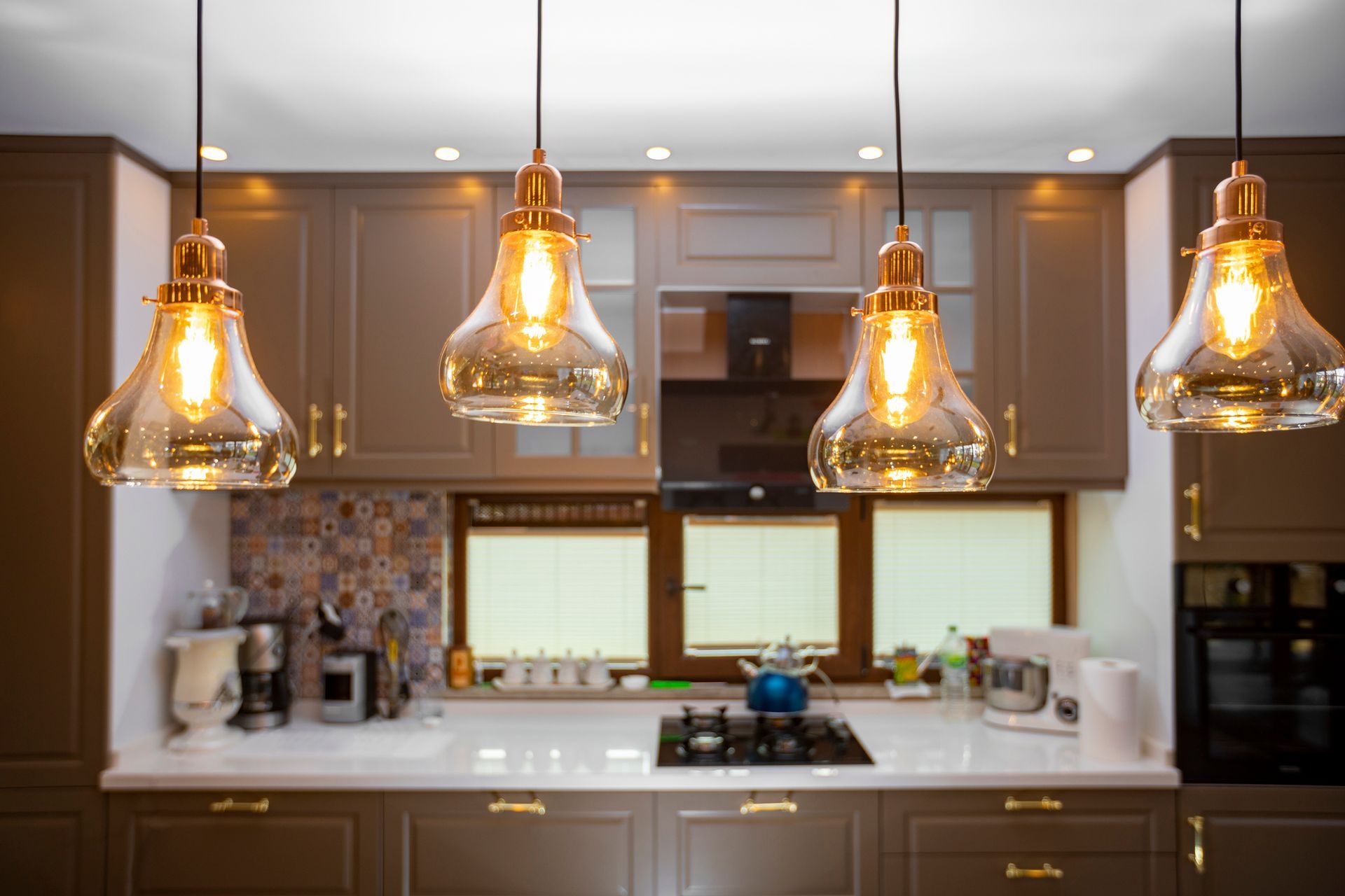 A kitchen with a stove , sink , cabinets , and pendant lights hanging from the ceiling.
