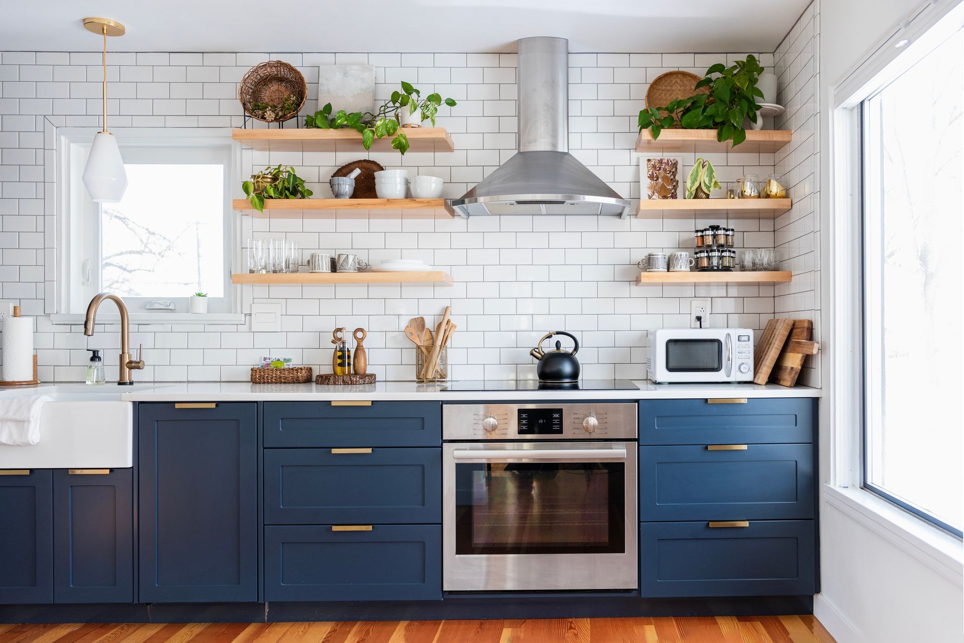 A kitchen with blue cabinets , stainless steel appliances , a sink , and a window.
