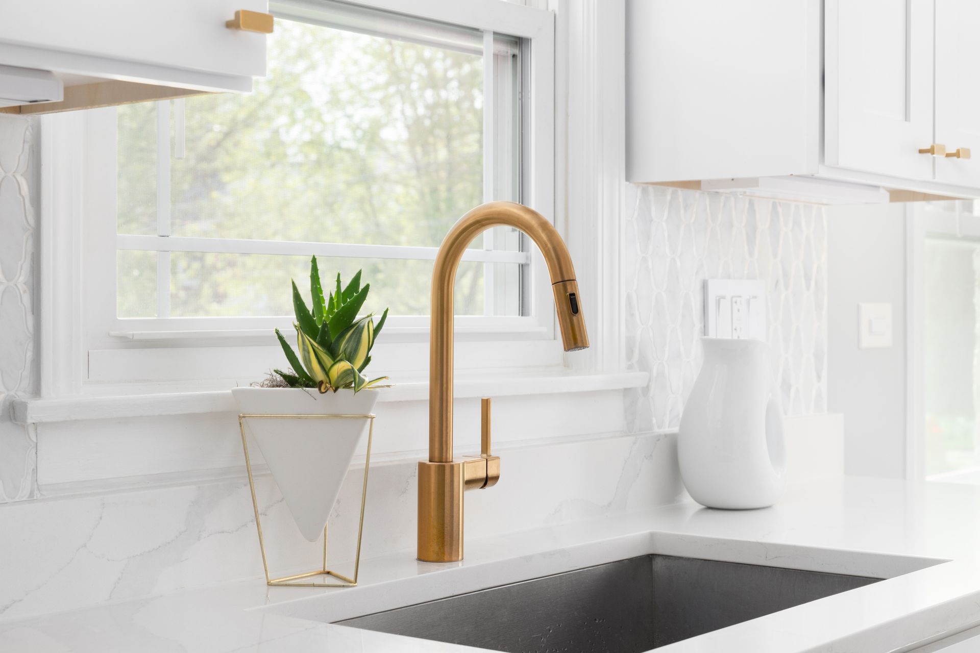 A kitchen sink with a gold faucet and a potted plant on the counter.