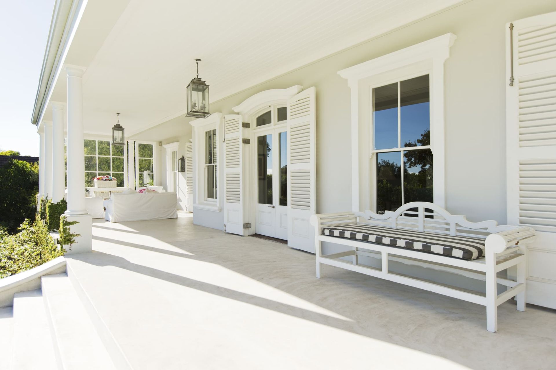 A white porch with a bench and shutters on it