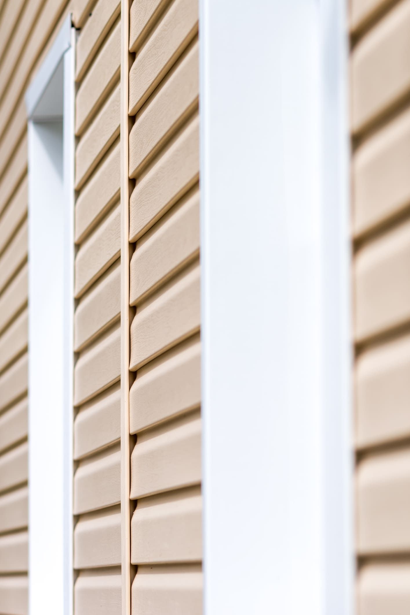 A close up of a house with beige siding and white windows.