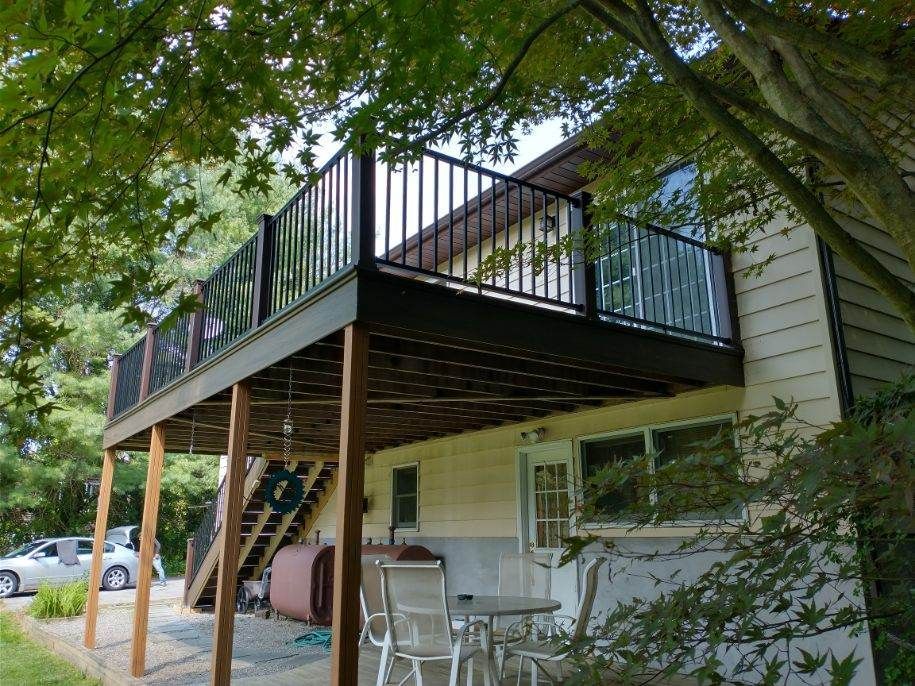 A large wooden deck with a black railing and trees in the background