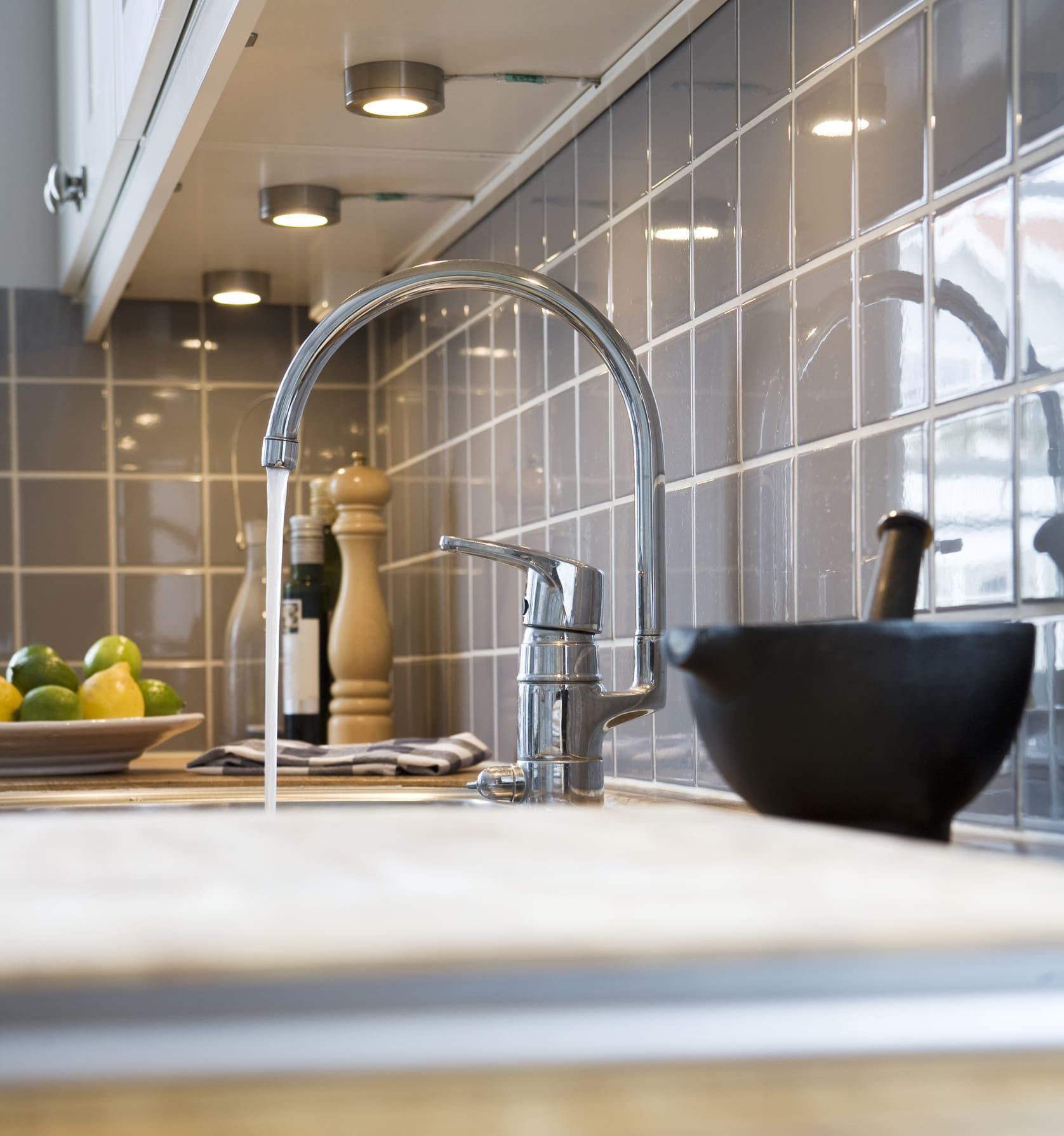 A kitchen sink with a bottle of wine in the background
