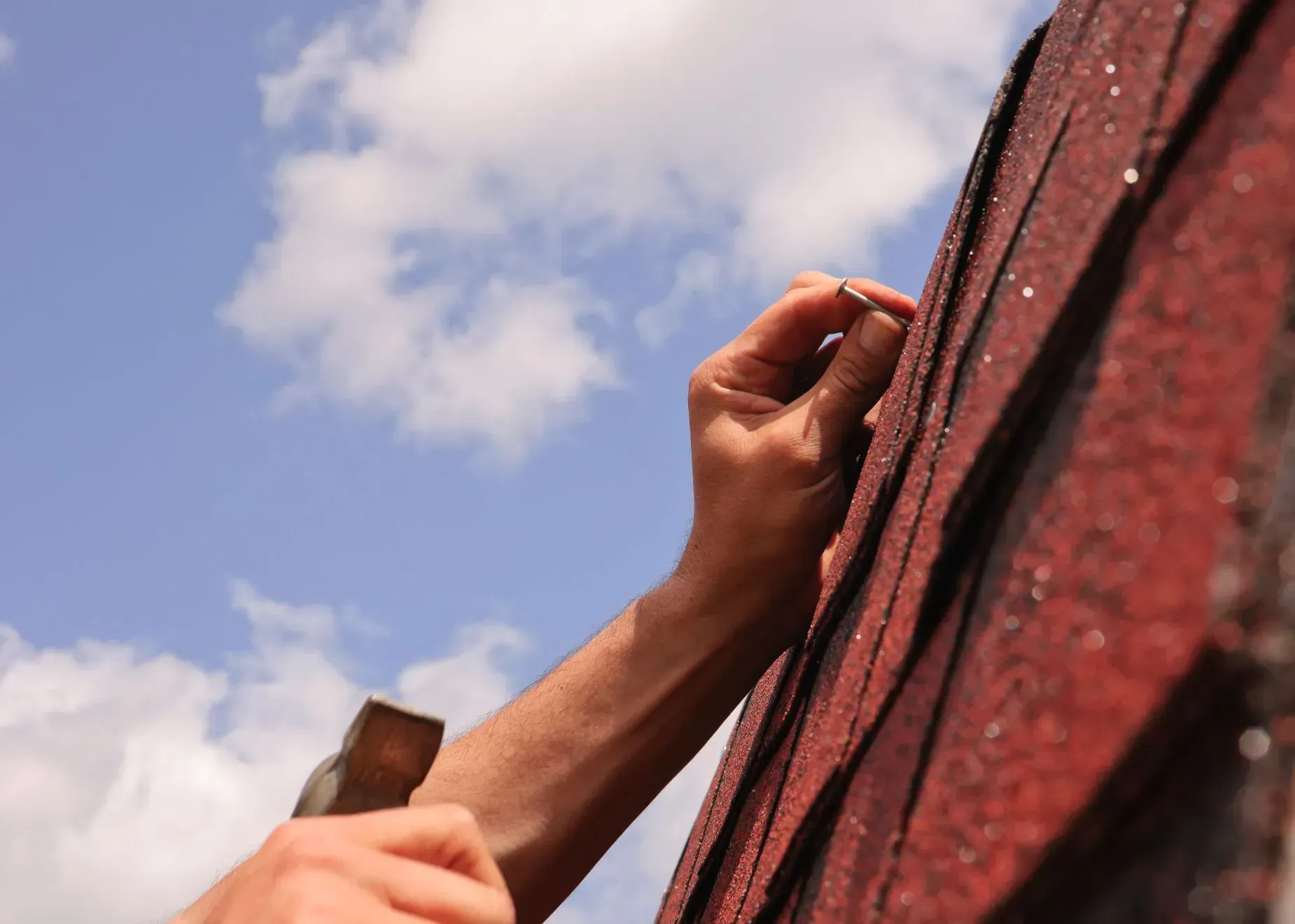 A person is hammering a nail into a red roof