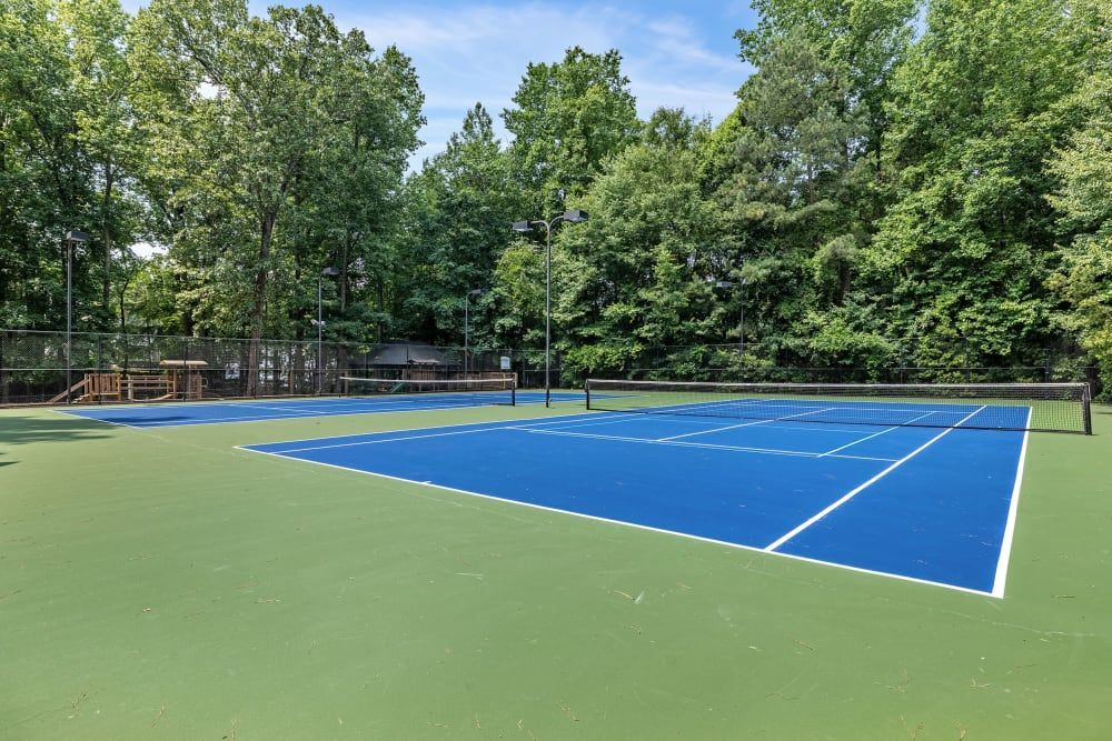 A tennis court surrounded by trees on a sunny day at Marquis at Sugarloaf in Duluth, GA.