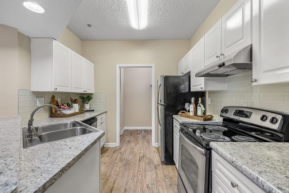 Apartment kitchen with white cabinets, stainless steel appliances, granite counter tops, a sink, and a refrigerator at Marquis at Sugarloaf in Duluth, GA.