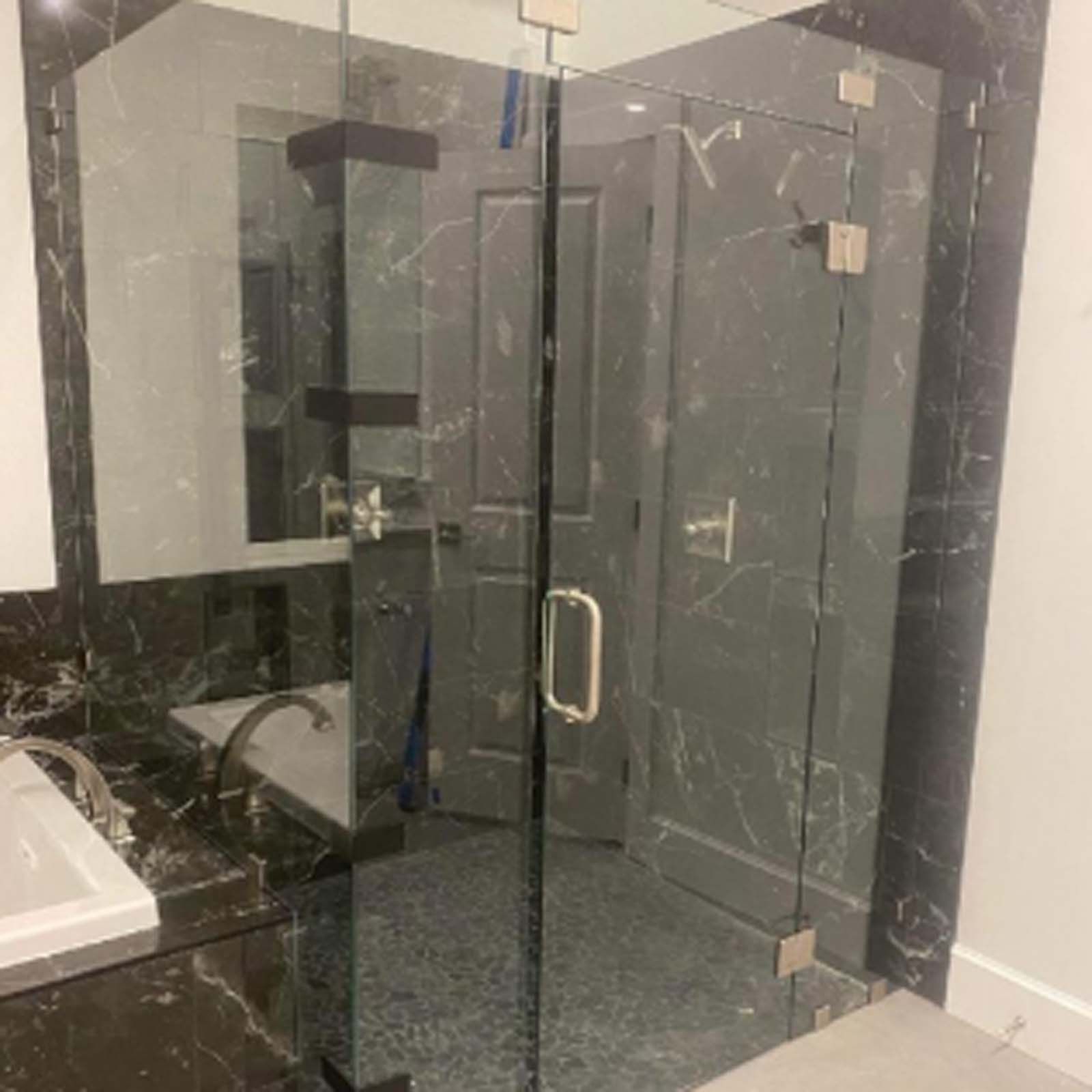 Bathroom with glass shower door, dark marble walls, and a white sink.