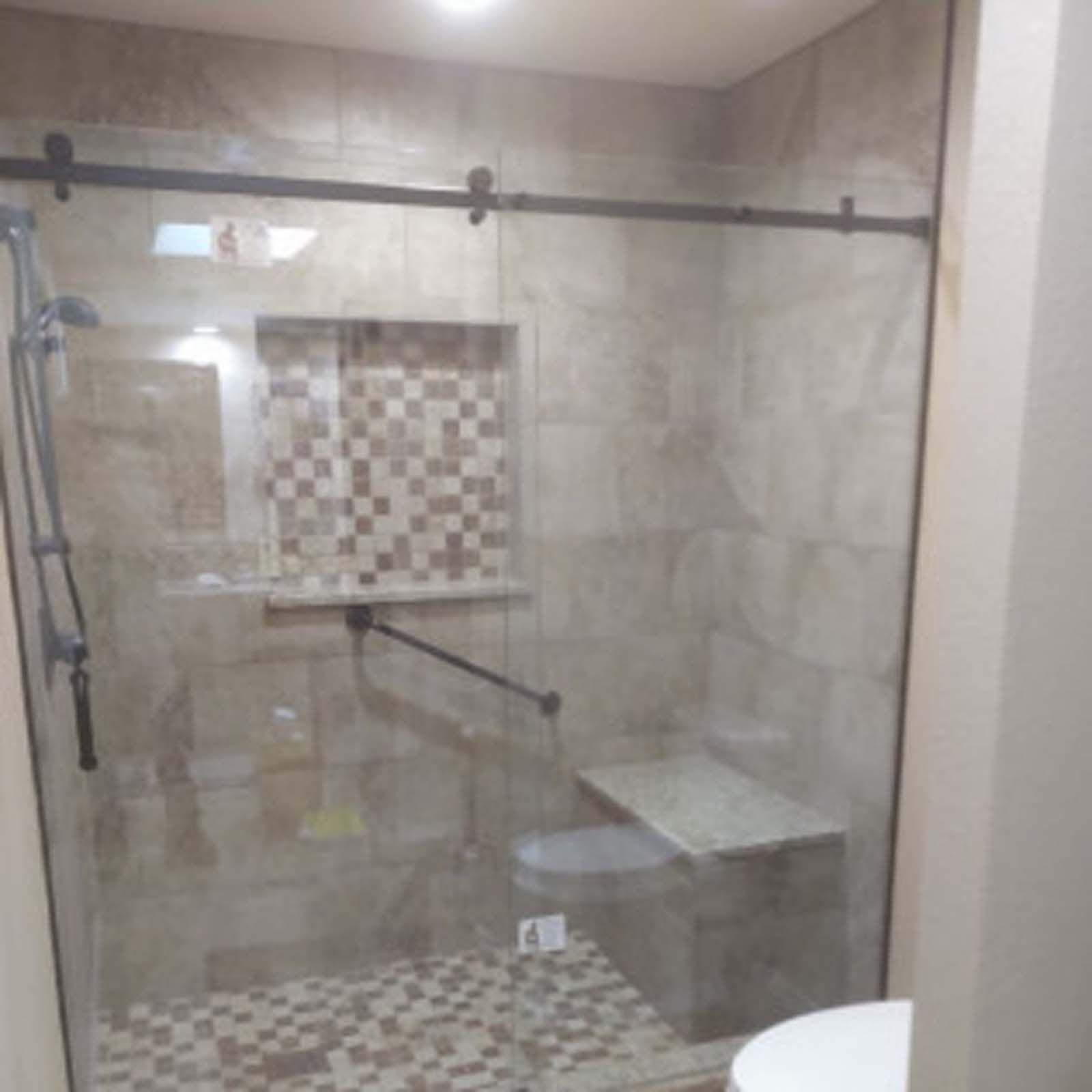 Shower with glass door, tiled walls, built-in seat, and grab bar.