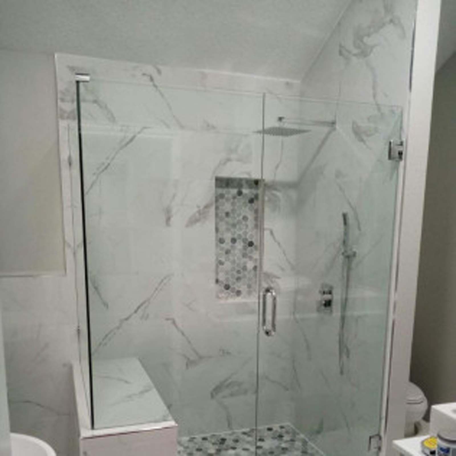 Glass shower enclosure with white marble tiles and built-in niche.