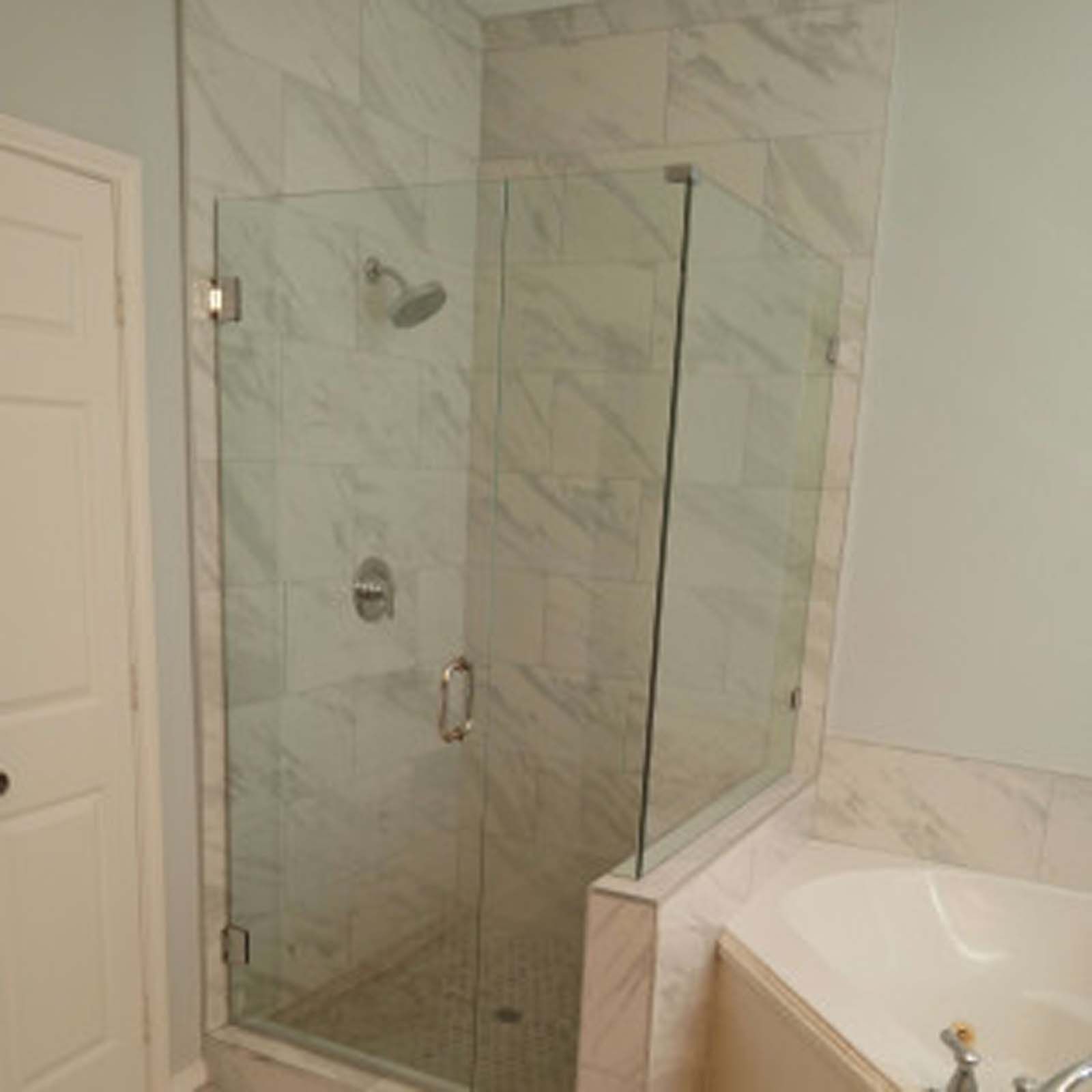 Glass shower enclosure with marble tile in a bathroom.