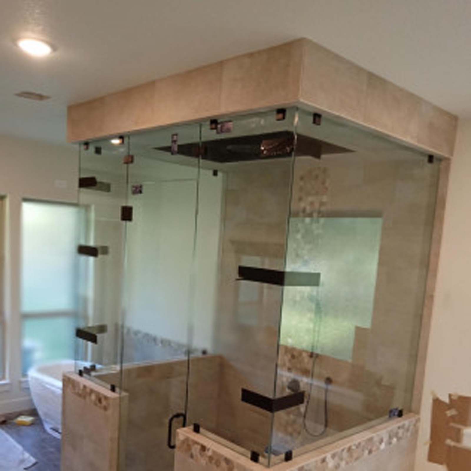 Frameless glass shower enclosure with beige tile and dark metal hardware.
