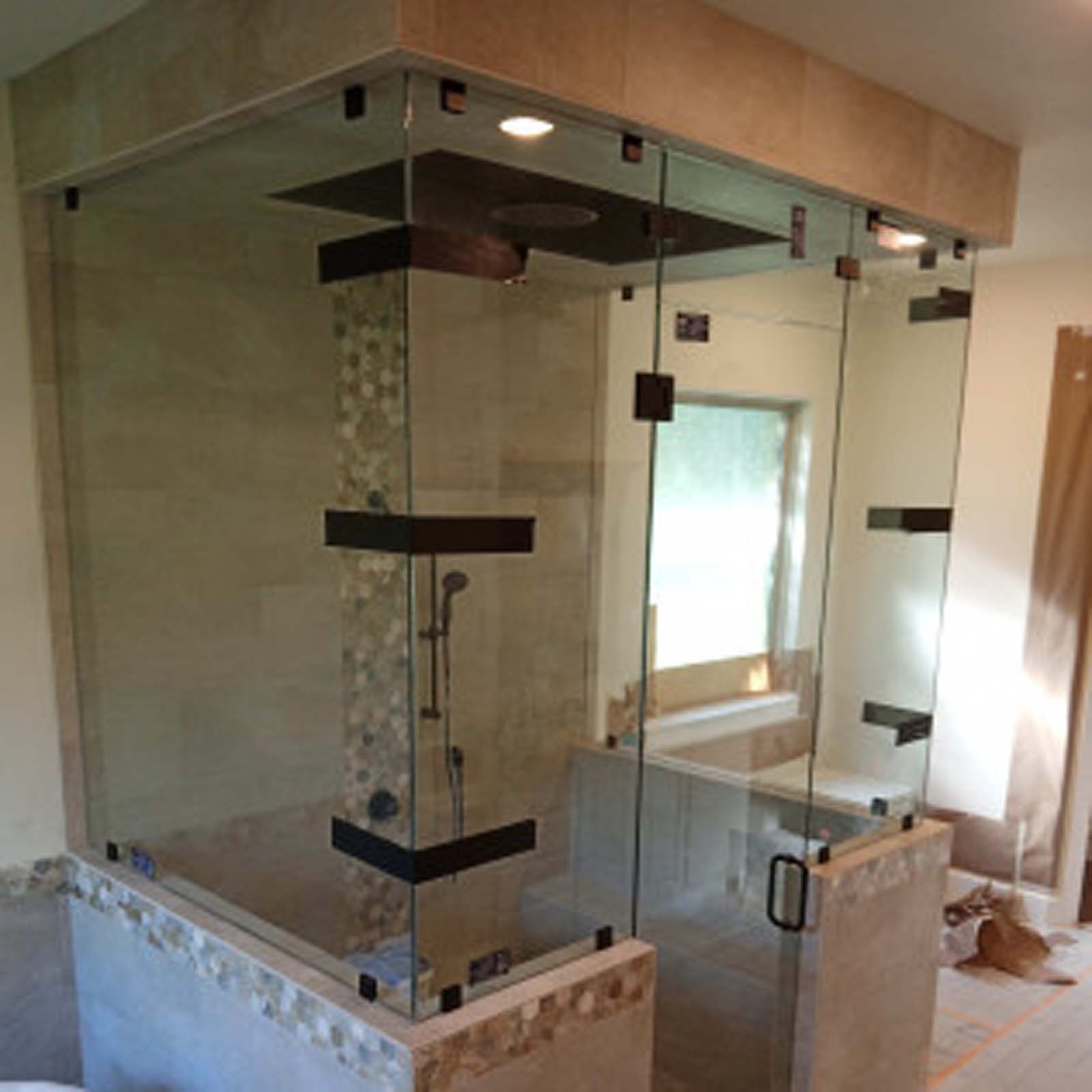 Glass shower enclosure with black hardware, beige tile walls, and a stone accent.