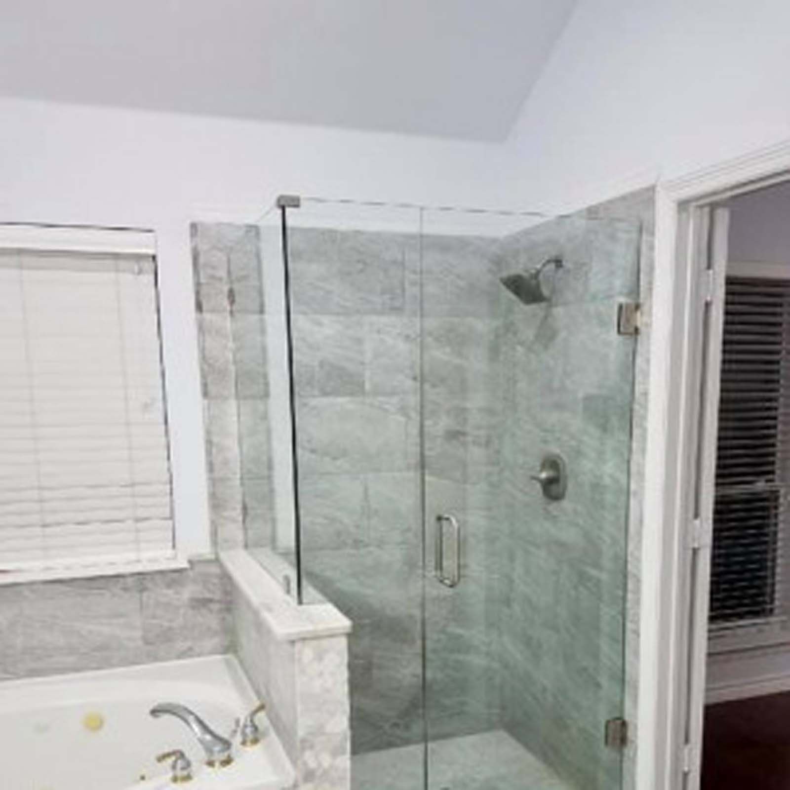 A modern bathroom with a glass shower enclosure and gray tiled walls. A bathtub is in the foreground.