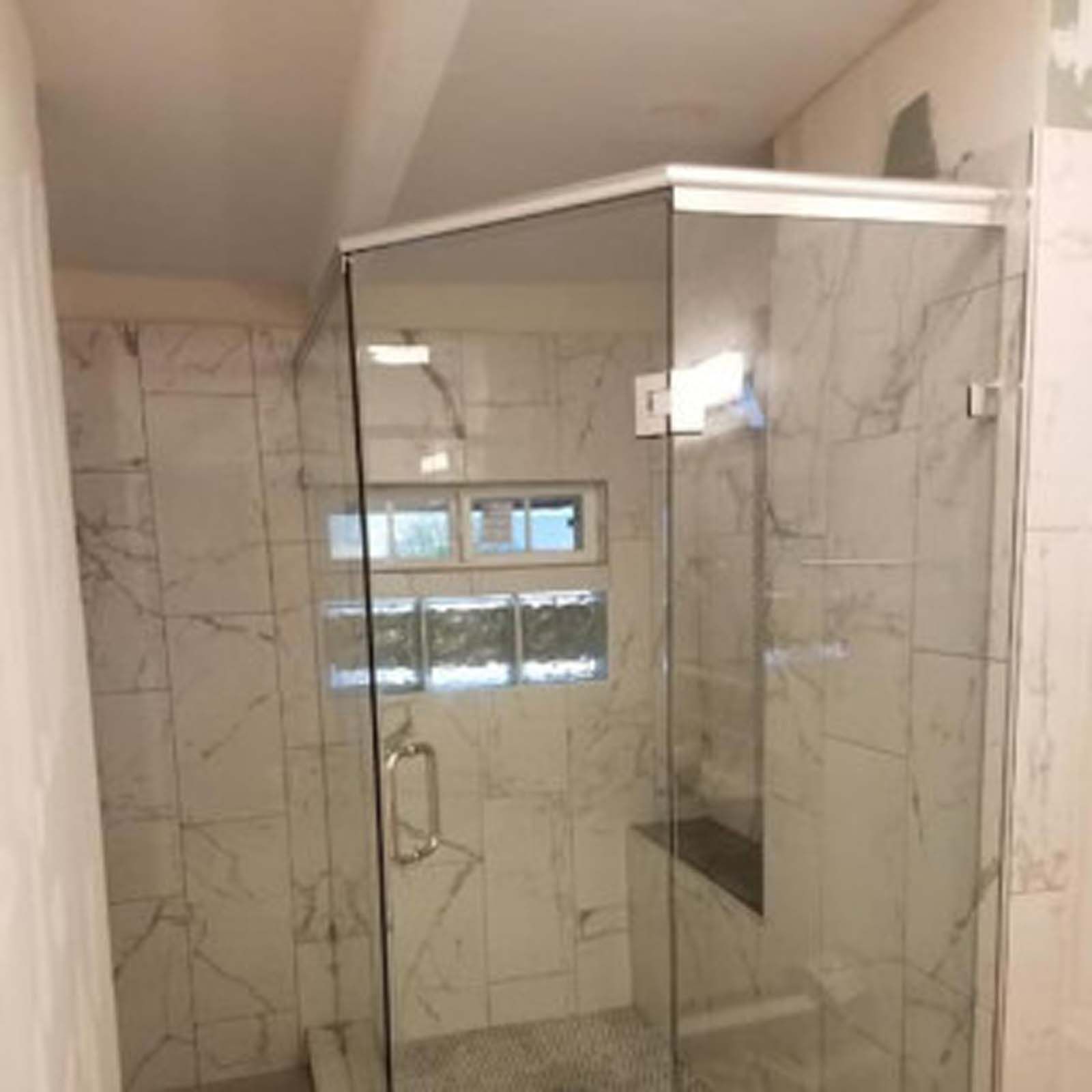 A frameless glass shower enclosure in a bathroom with white marble tile.