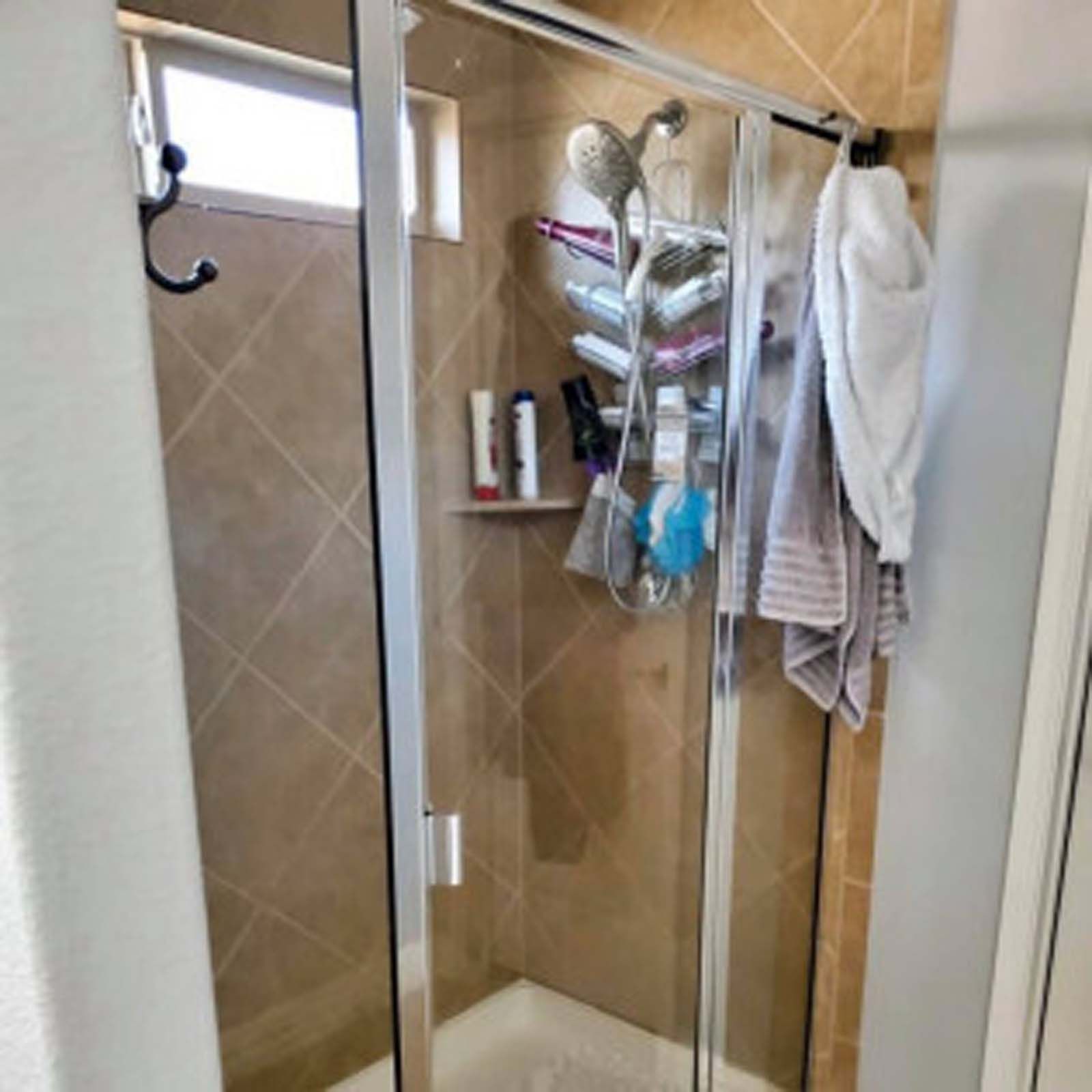 Shower with glass sliding doors, beige tiled walls, and various toiletries and towels.