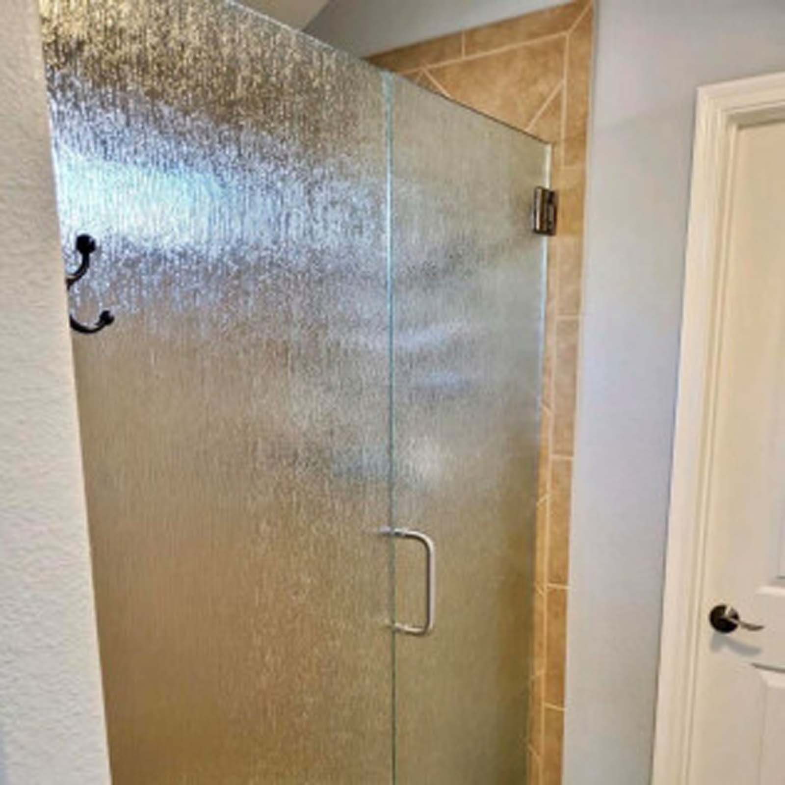 Textured glass shower door in a bathroom, with a chrome handle and hinges. Brown tile is visible on the adjacent wall.