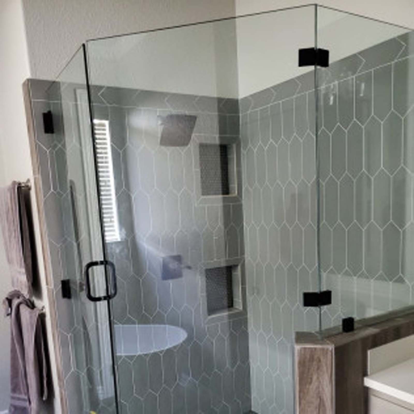 Glass-walled shower with gray tile, black hardware. Towel rack and window visible.