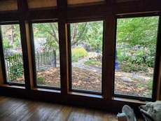Three rectangular windows offer a view of a lush garden with a winding path. A dog and a fan are in the foreground.