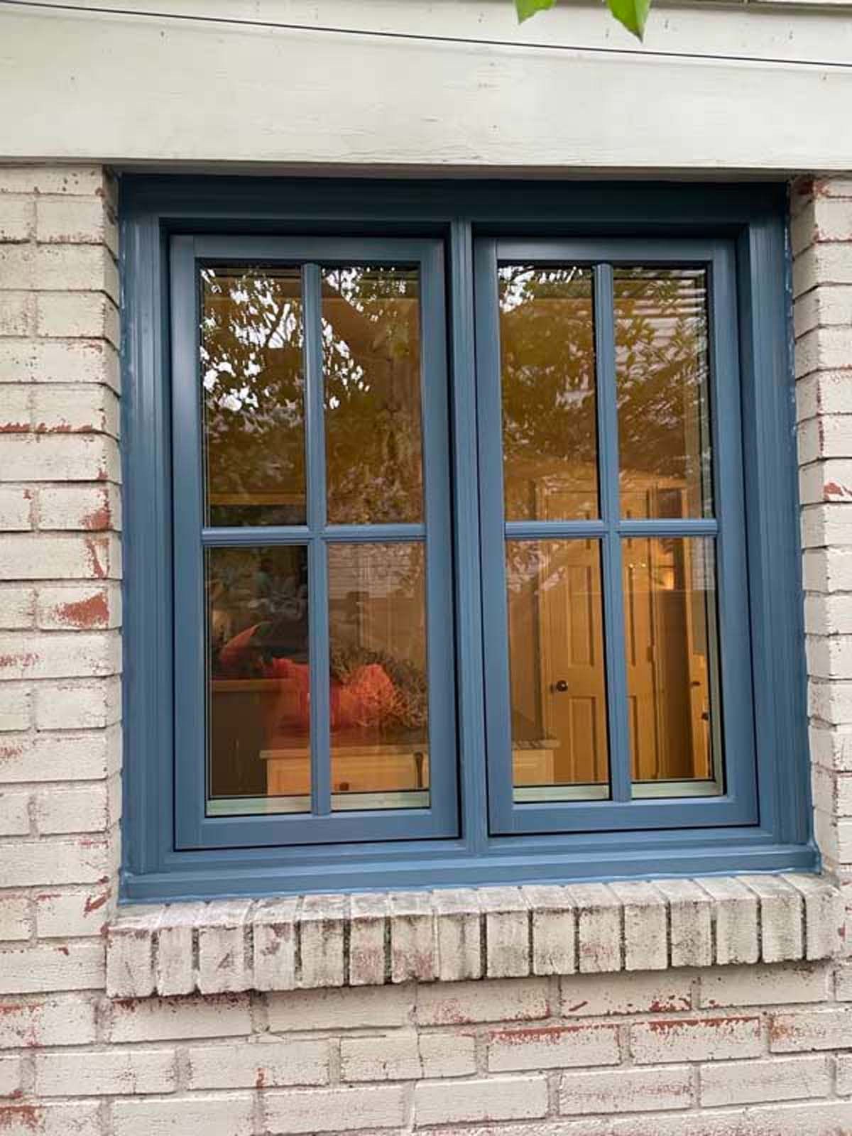 Blue-framed window with six panes, set in a brick wall. Reflections show interior objects and a wooden door.