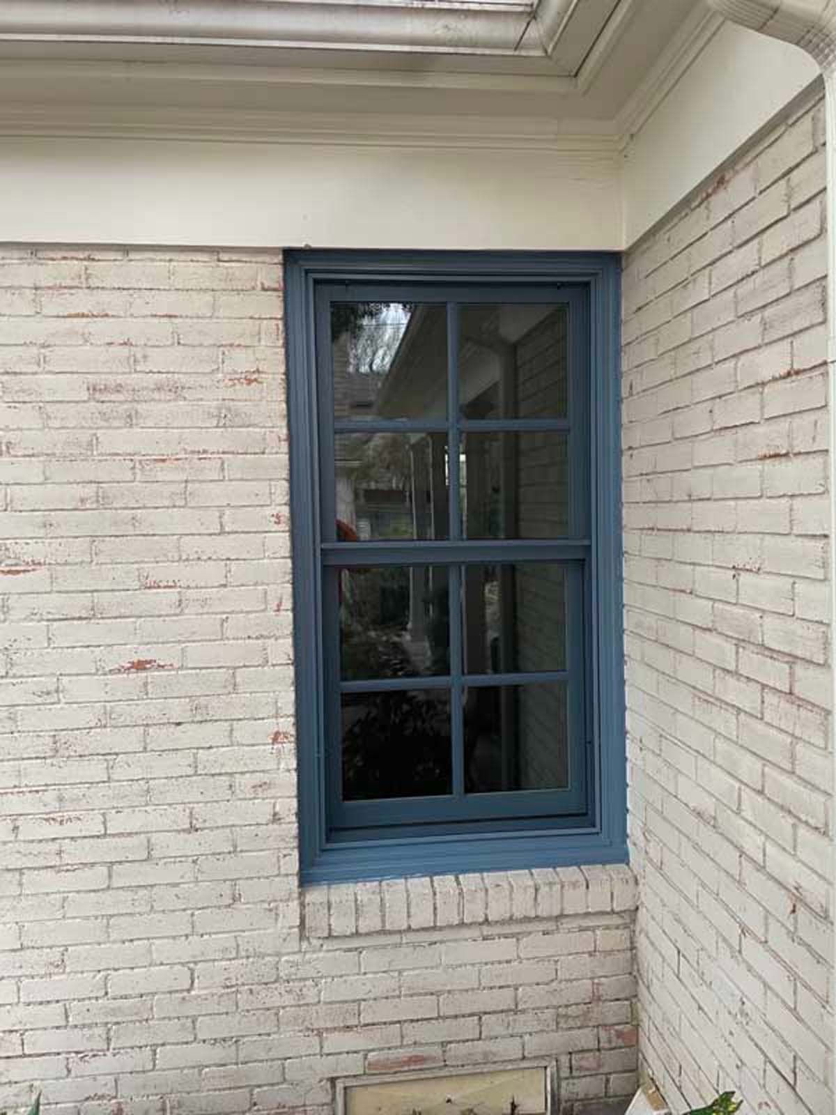Blue-framed window on a white brick wall. The window is above an opening in the brick.