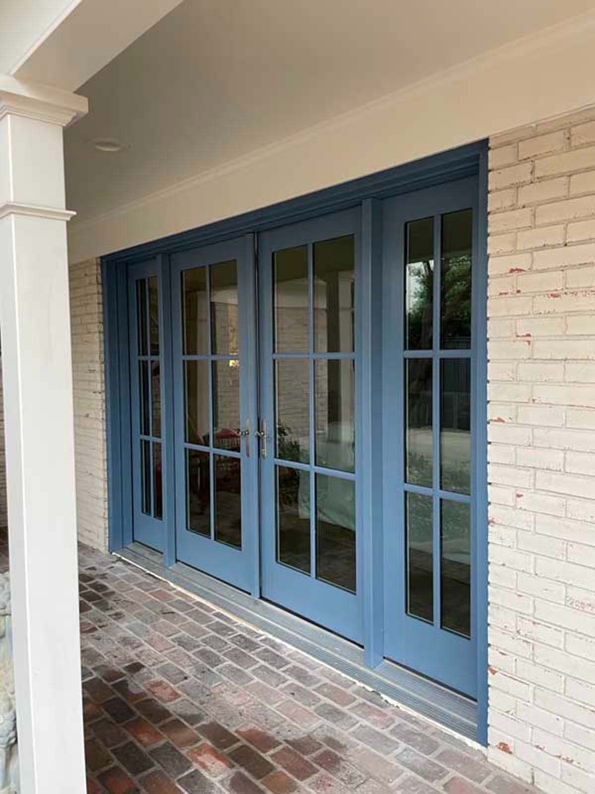 Blue French doors on a brick patio, set in a white-painted porch, with a white pillar.