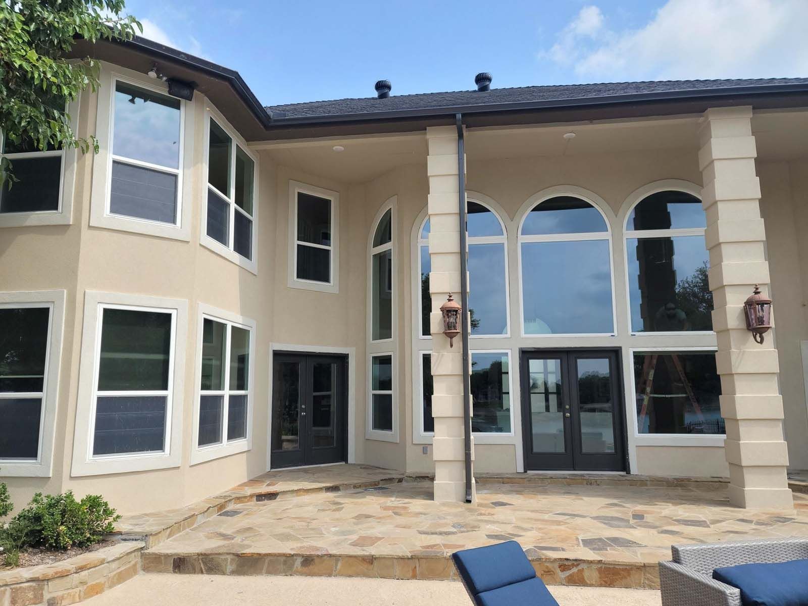 Beige stucco house with large windows, dark roof and doors, and stone patio.