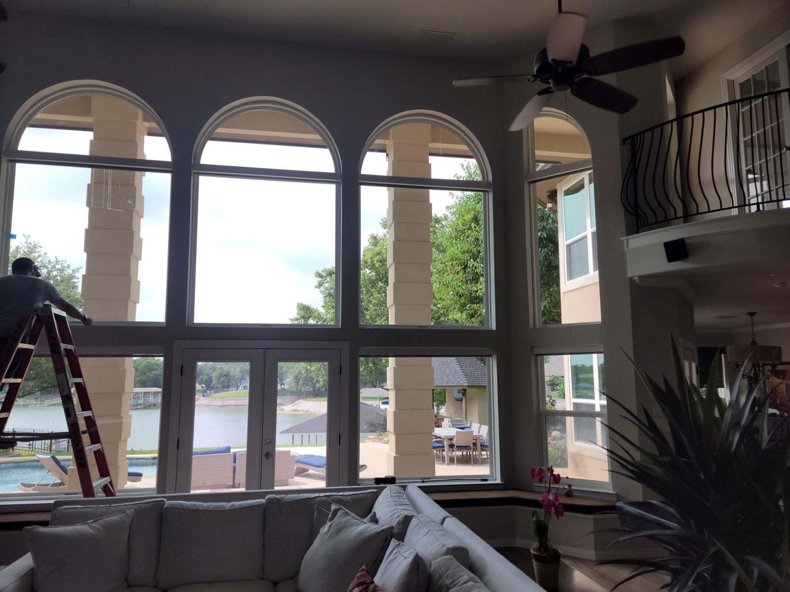 Man on ladder cleaning large arched windows overlooking a lake.