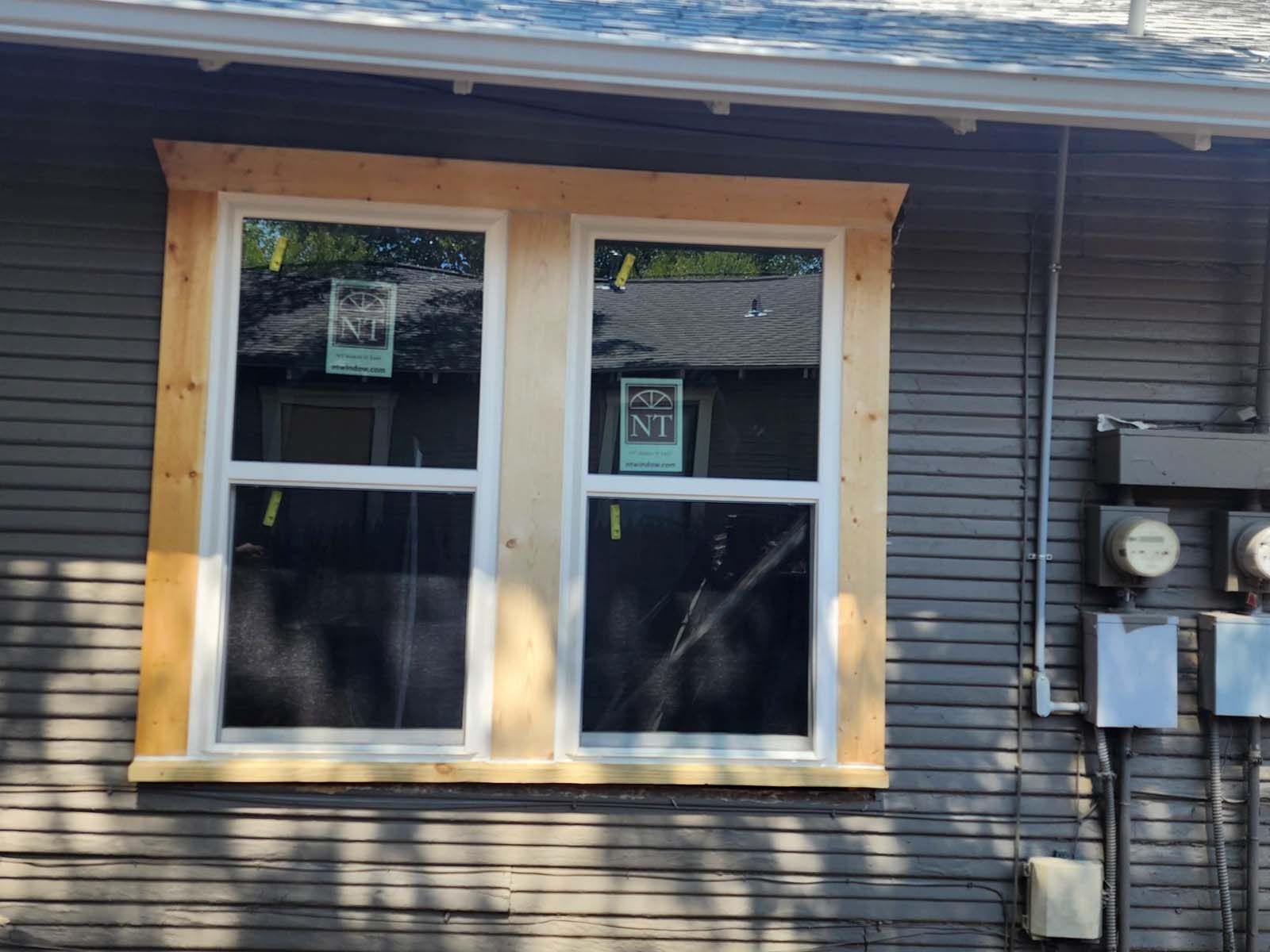 Newly installed double window in a grey-sided house, surrounded by unfinished wood trim.