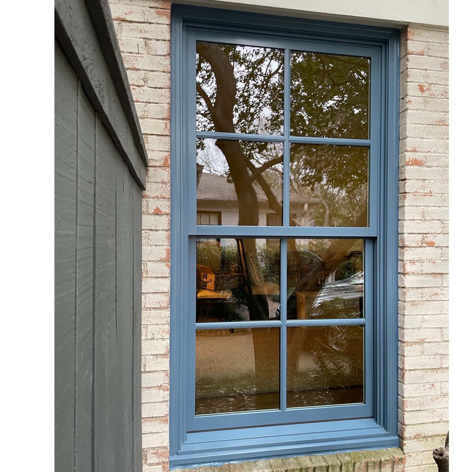 Blue-framed window on a brick building reflects a tree. Next to gray siding.