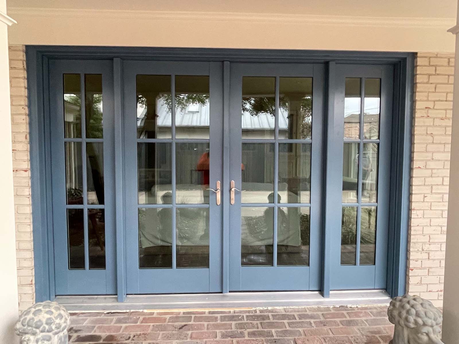 Blue French doors with glass panes, framed by brick and painted trim.