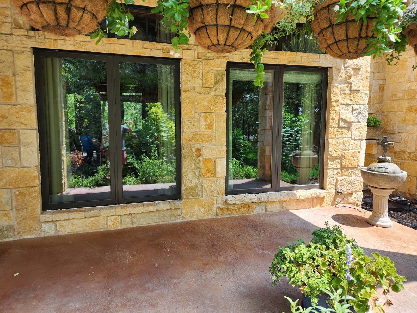 Two windows with dark frames set in a tan stone wall, beneath hanging baskets.