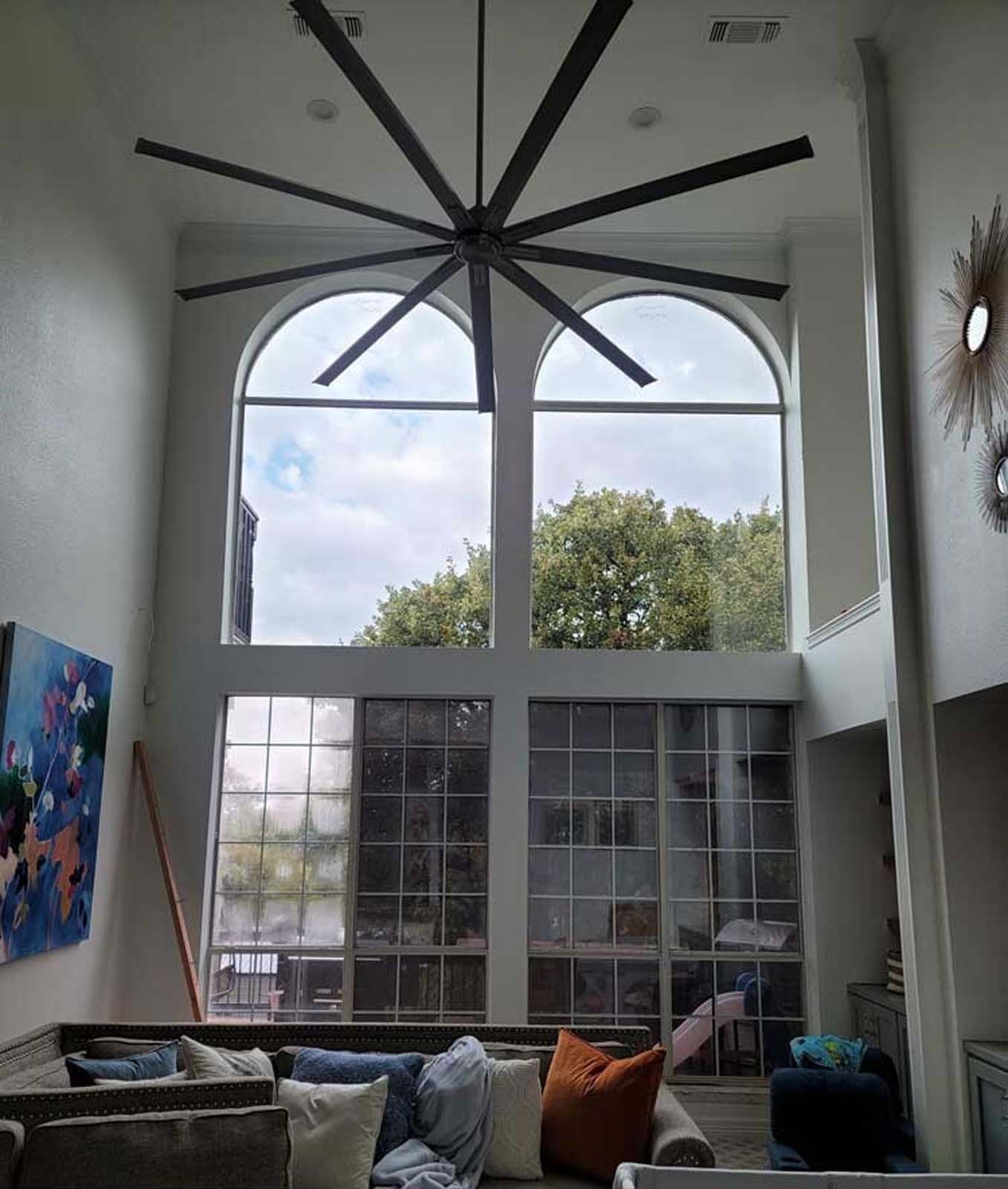 High-ceiling living room with large windows, a giant fan, and a couch.