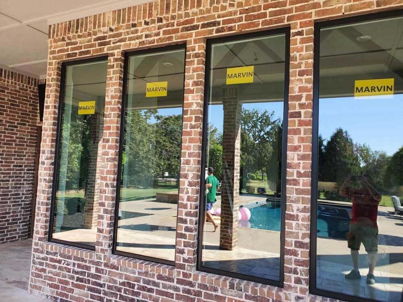 Brick wall with four tall windows; a pool and trees are reflected in the glass.