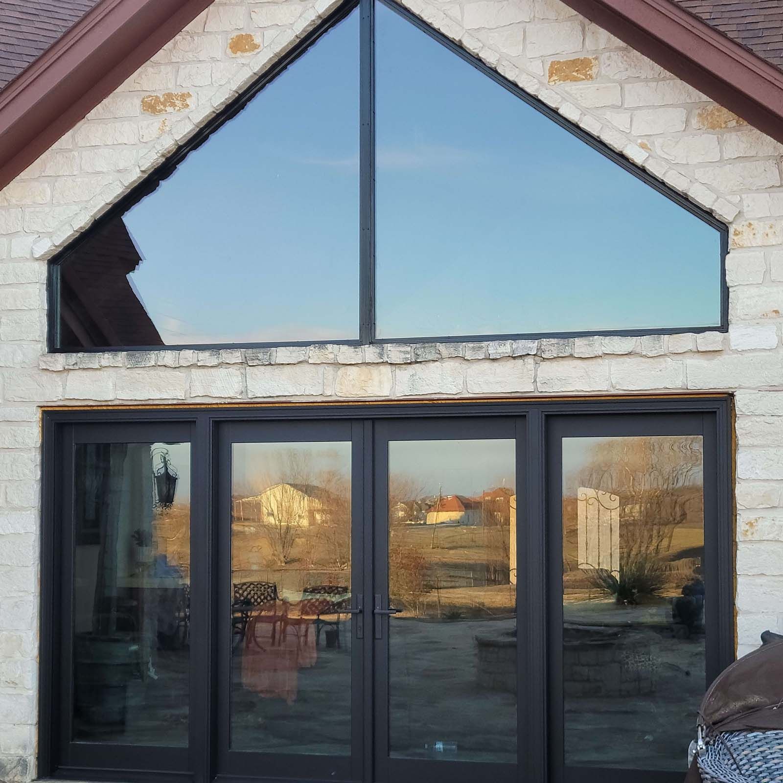 House exterior with large triangular window above black framed doors, reflecting outdoor scene.