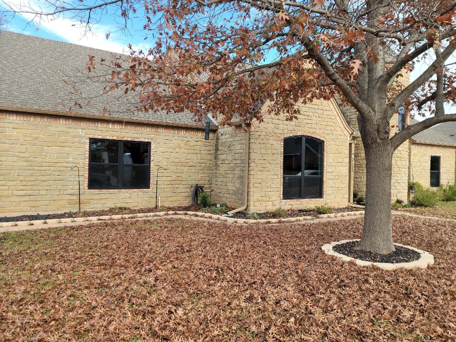 Tan brick building with dark windows and a tree with brown leaves in front.