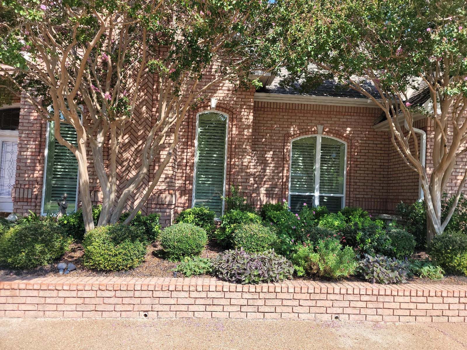 Red brick house with landscaped front yard, trees, bushes, and shuttered windows.