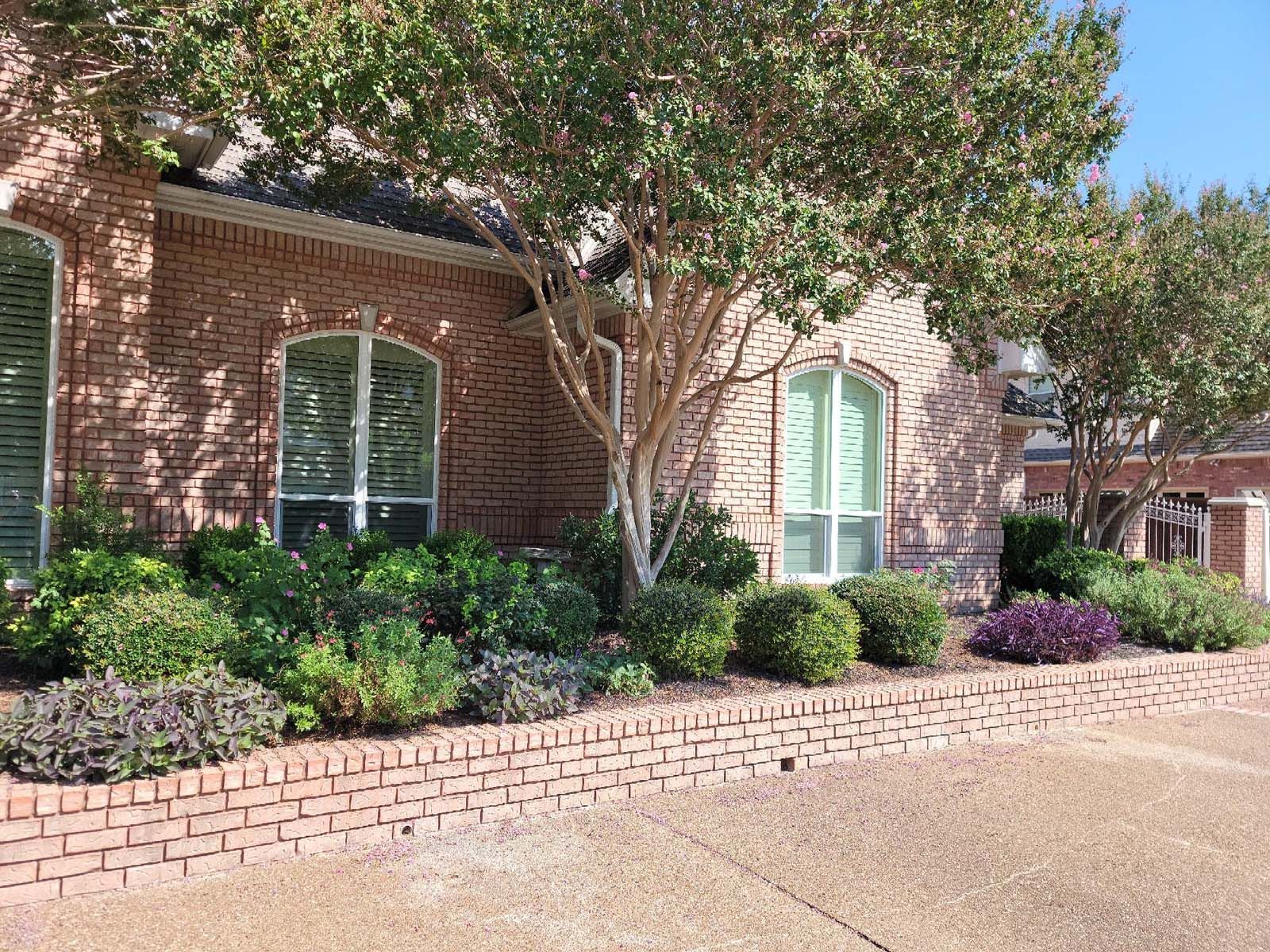 Brick house with arched windows, landscaped yard, and trees.