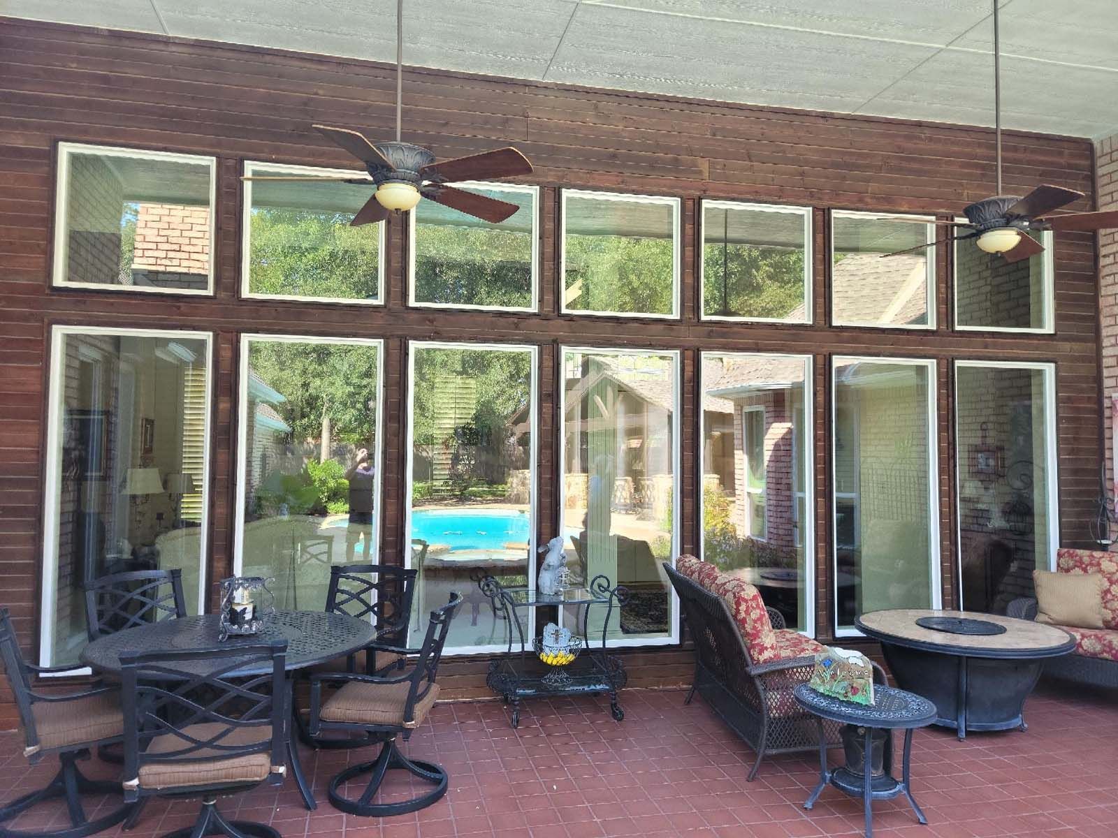 Patio with multiple windows overlooking a pool. Brown brick wall, ceiling fans, outdoor furniture.