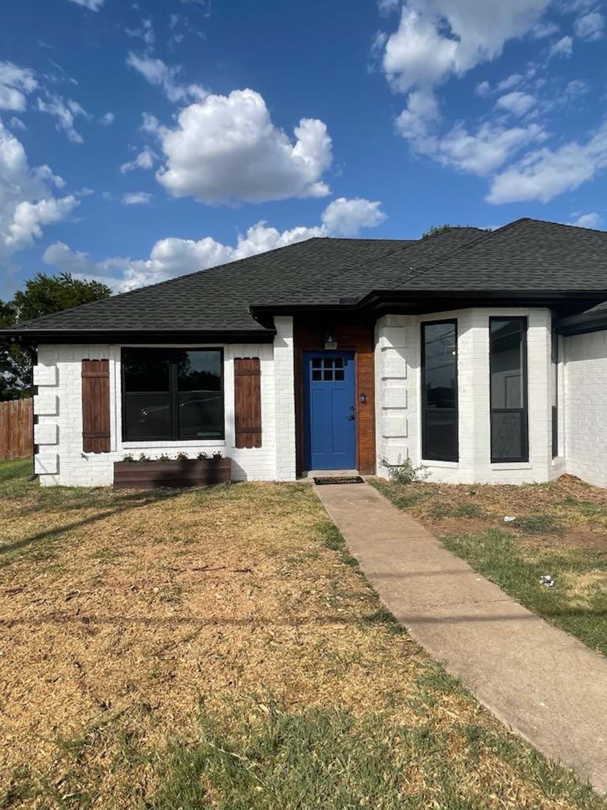 White brick house with blue door and brown shutters under a blue sky.