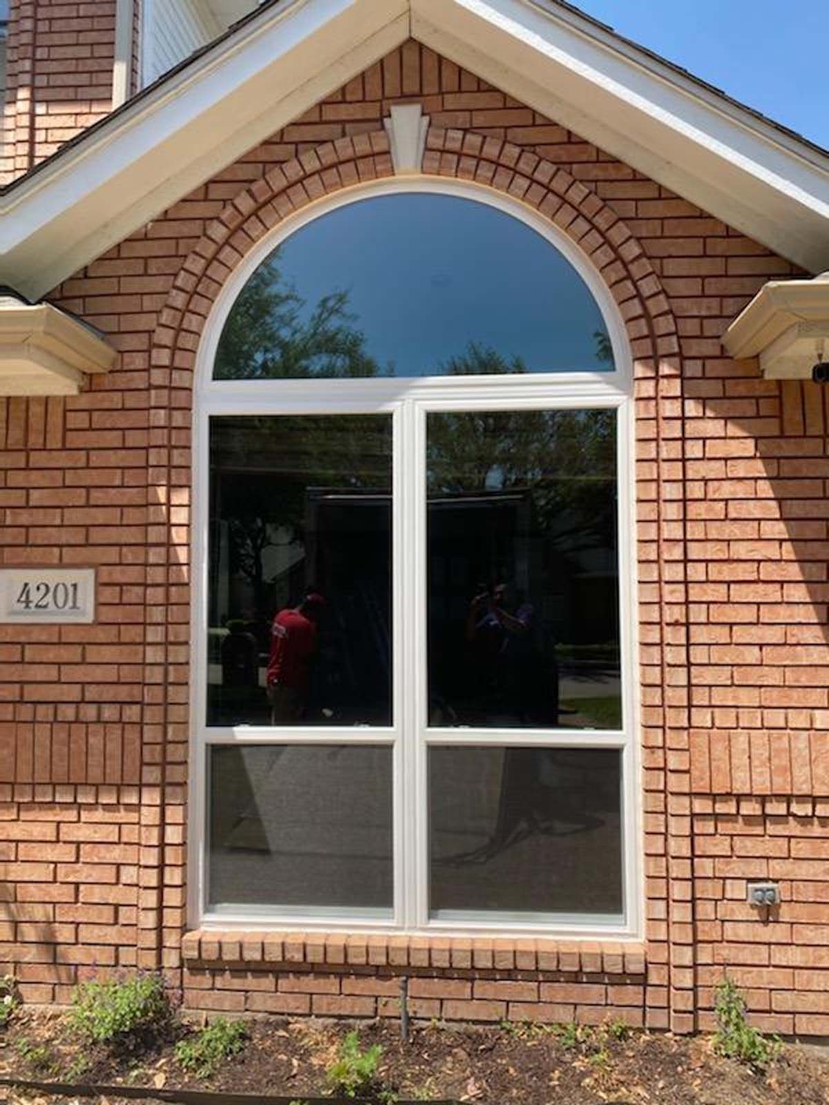 Brick building with arched window. White-framed window with tinted glass. Address number 
