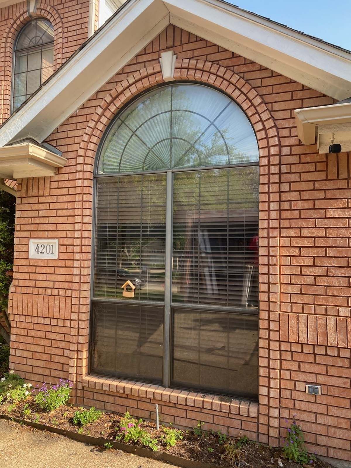 Red brick house with large arched window, blinds, and address 