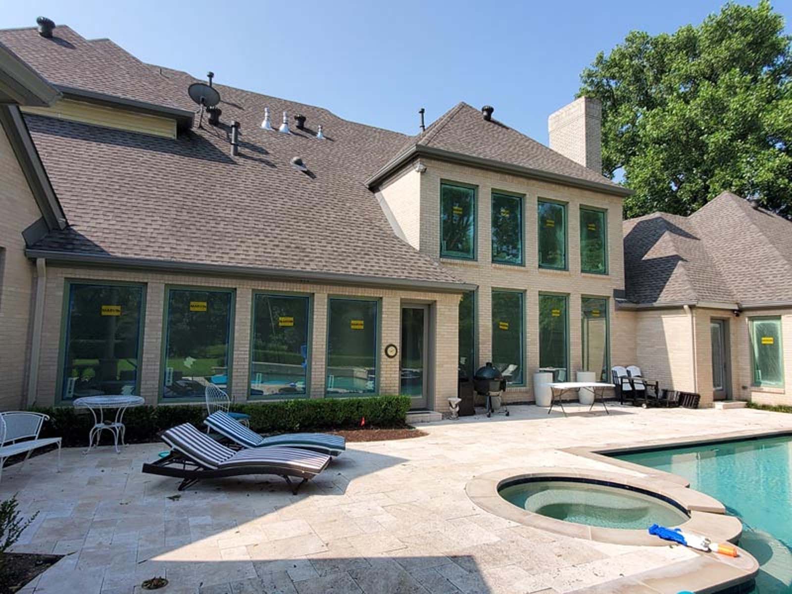 Backyard with pool, patio, and house with large windows.