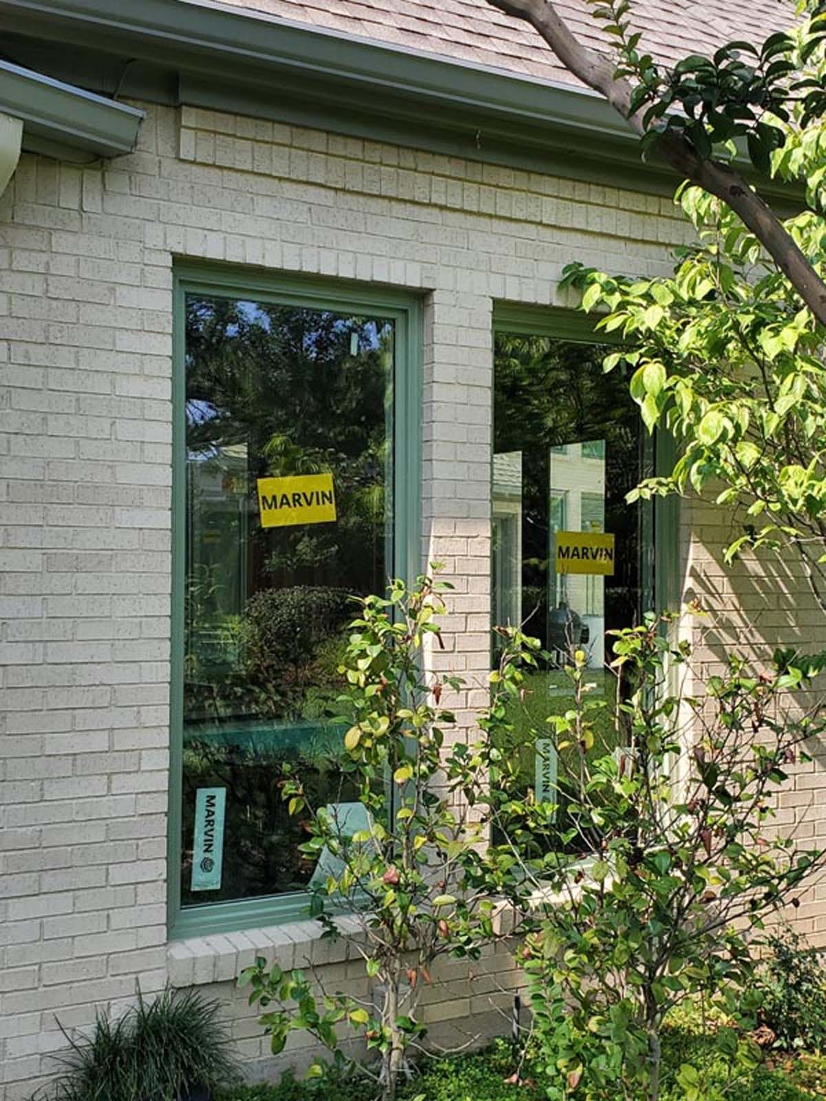 Brick building exterior with two windows. Green trim, yellow signs visible. Plants in front.