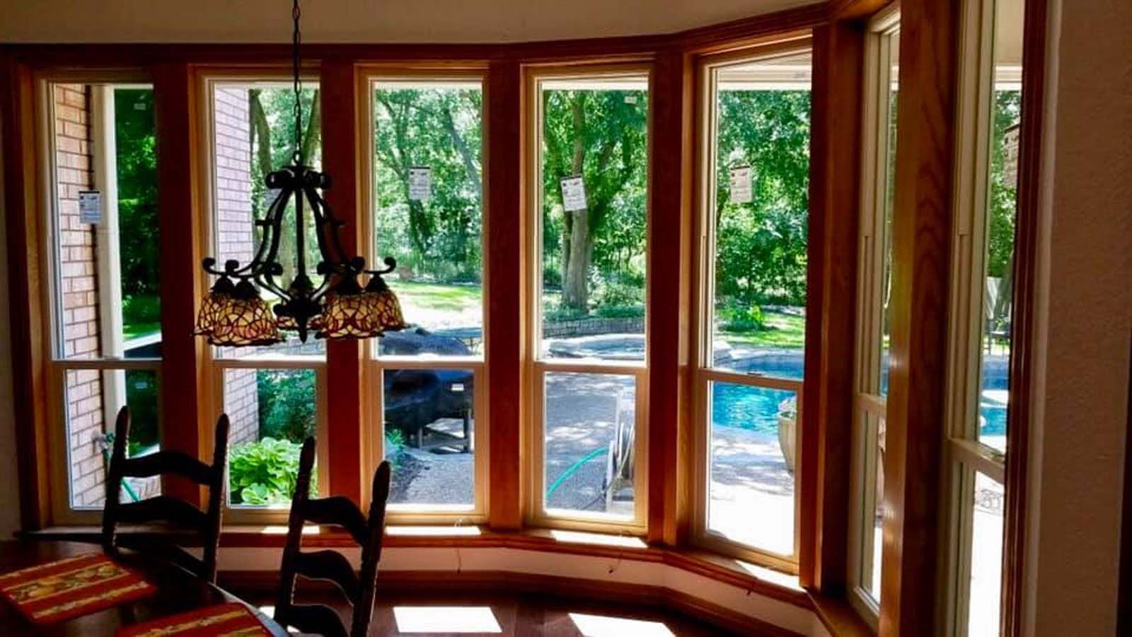 Dining room with bay windows overlooking a backyard with a pool. Dark wood trim and a chandelier.