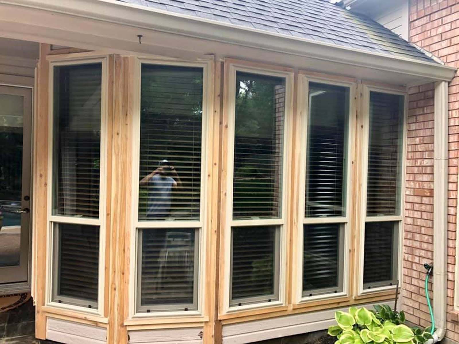 A sunroom with large windows, light wood trim, and blinds reflecting the outdoors, attached to a brick house.