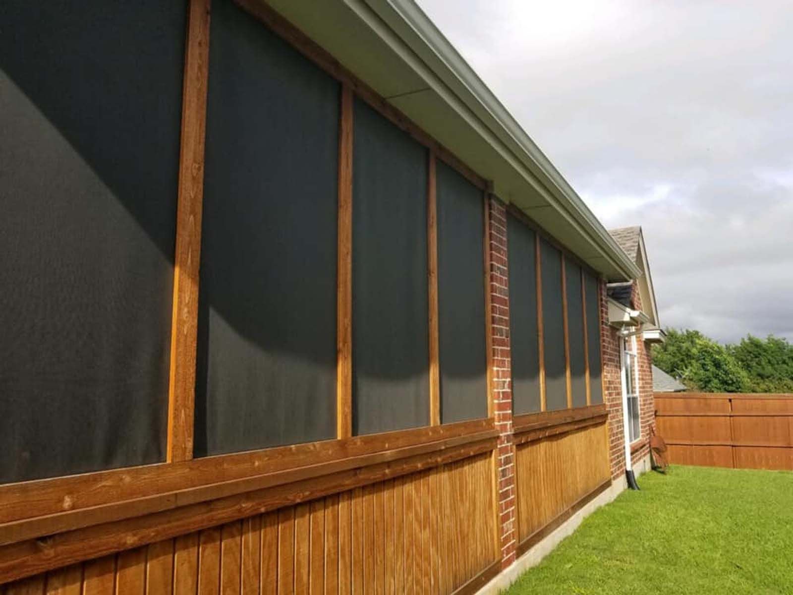 Screened-in porch on a house with dark screens, brown wood framing, brick accents, and a gutter, with green grass in yard.